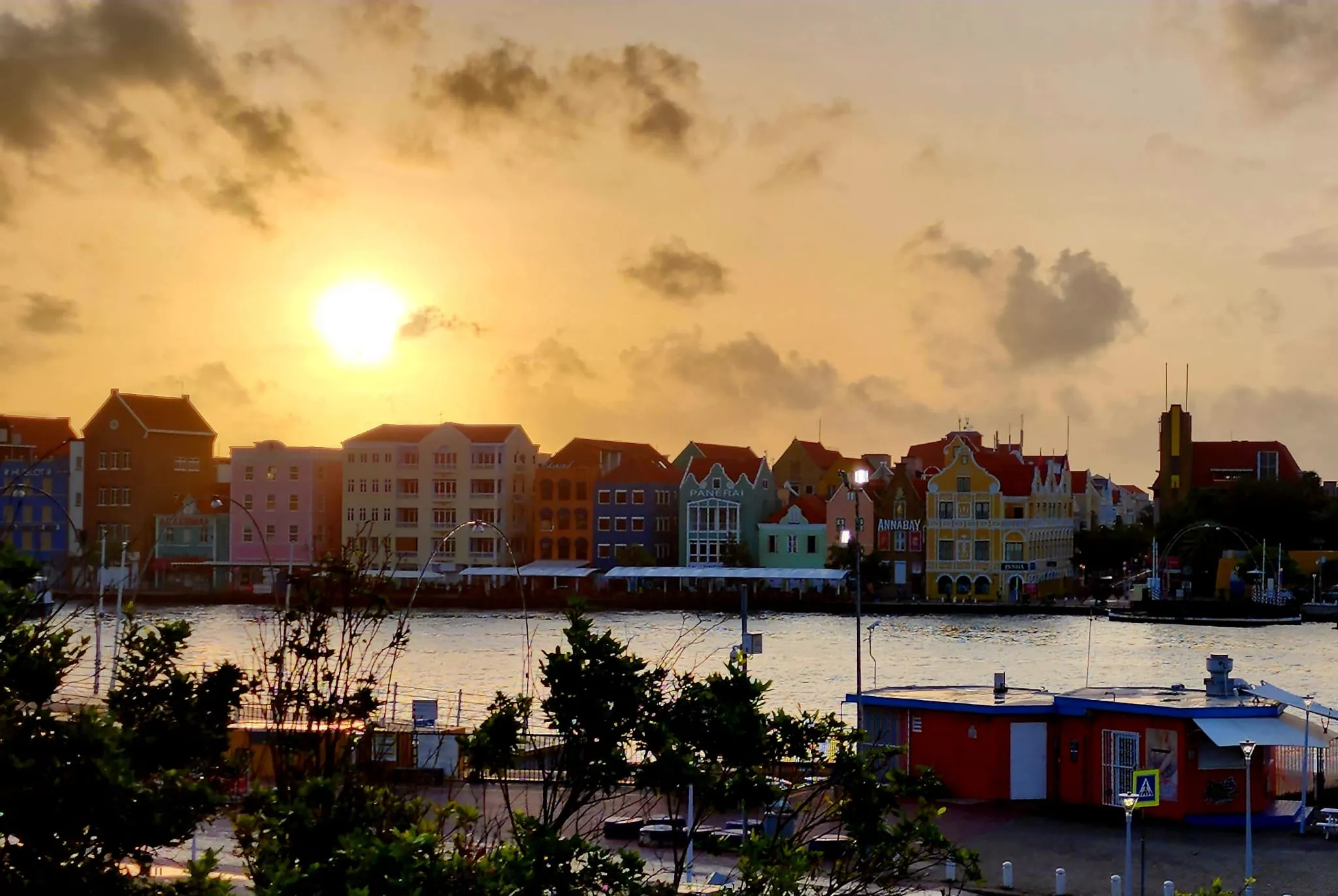 The Willemstad waterfront at golden hour, the whole pastel row glowing under a low, warm sun.